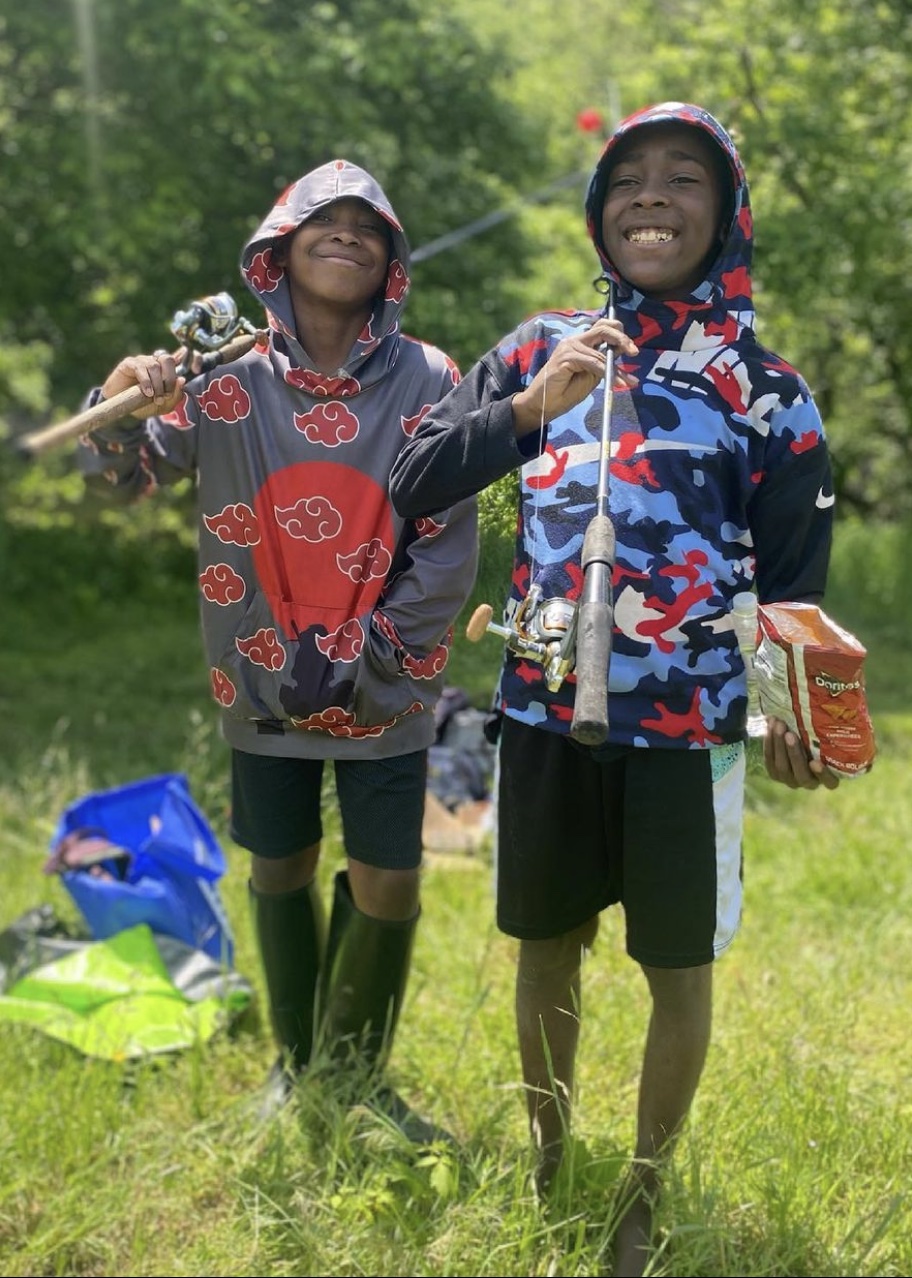 Two boys stand with fishing gear and smile big at the camera